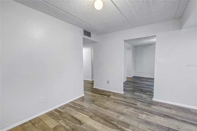 empty room featuring a textured ceiling, wood finished floors, visible vents, and baseboards