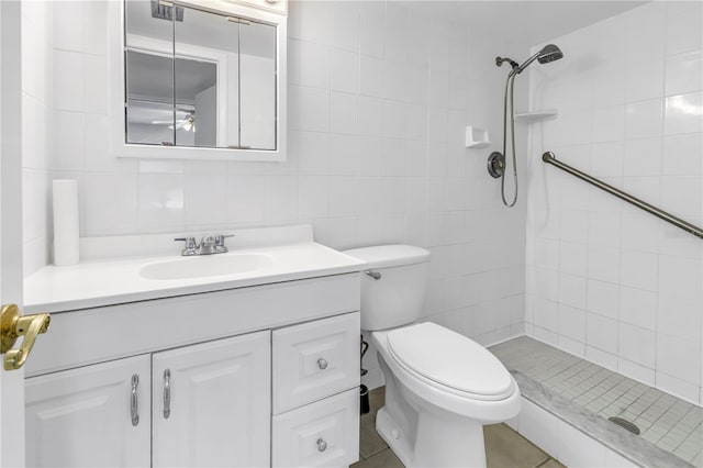 bathroom with vanity, tile walls, toilet, and a tile shower