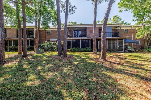 back of house with brick siding, a balcony, a yard, and a sunroom