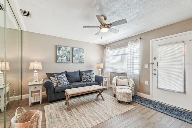 living room with visible vents, a ceiling fan, a textured ceiling, wood finished floors, and baseboards