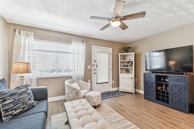 living area featuring light wood-style flooring, a ceiling fan, baseboards, and a textured ceiling