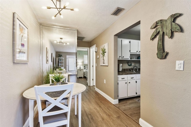 hall featuring a sink, visible vents, a chandelier, and light wood finished floors