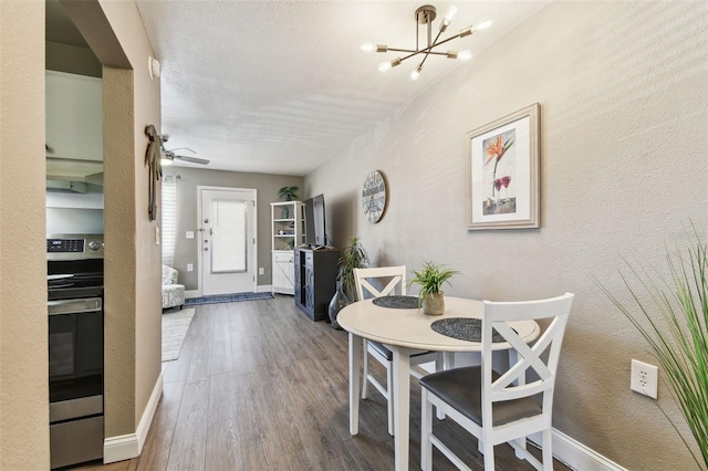 dining space with an inviting chandelier, wood finished floors, and a textured wall