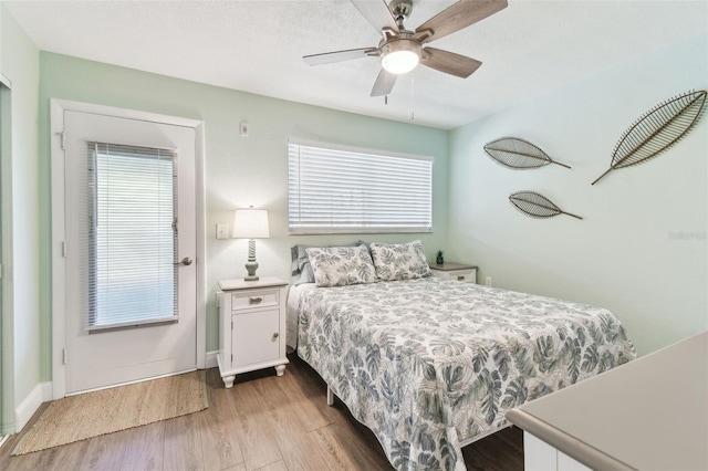 bedroom featuring baseboards, multiple windows, wood finished floors, and a ceiling fan