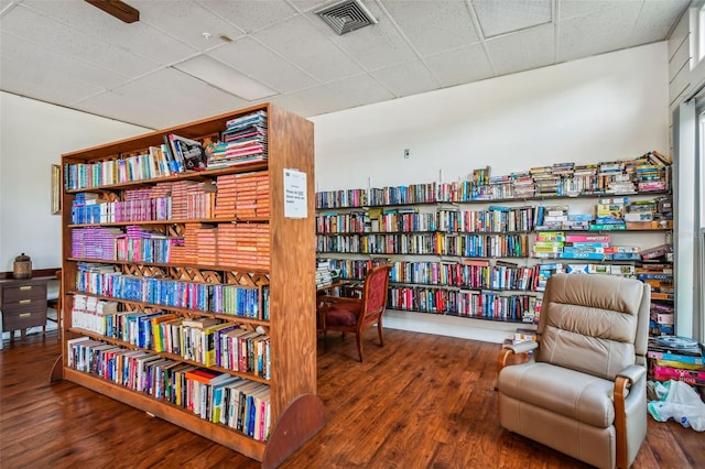 sitting room with bookshelves, visible vents, a drop ceiling, and wood finished floors