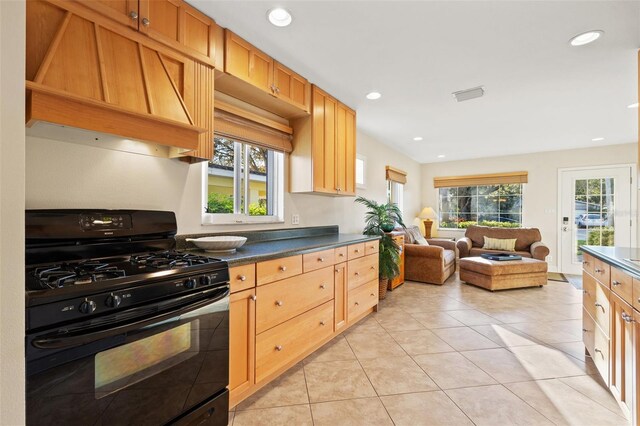 kitchen featuring black gas range oven, light tile patterned floors, dark countertops, and a wealth of natural light