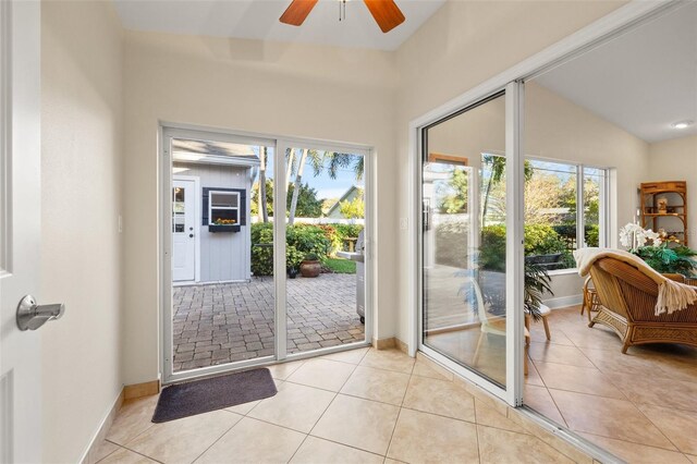 doorway featuring light tile patterned floors, a ceiling fan, baseboards, and vaulted ceiling