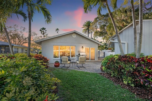 rear view of property featuring a patio area, stucco siding, a lawn, and fence