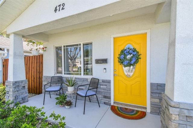 doorway to property with stone siding, stucco siding, and a porch