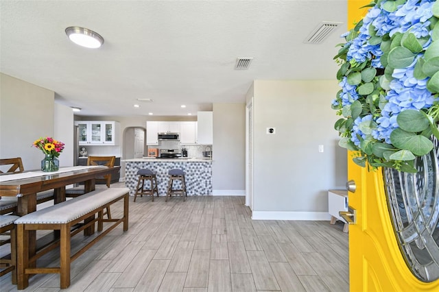 dining area with baseboards, arched walkways, visible vents, and wood finish floors