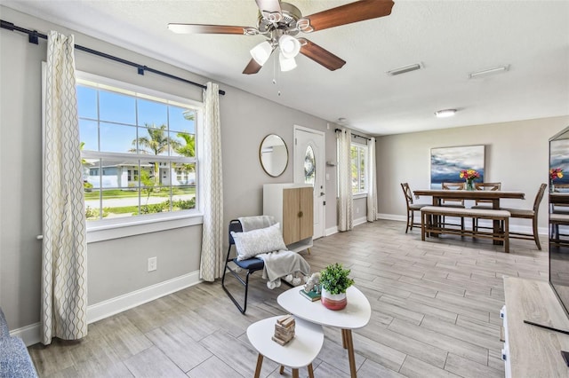 living area featuring light wood-style flooring, a ceiling fan, baseboards, and a textured ceiling