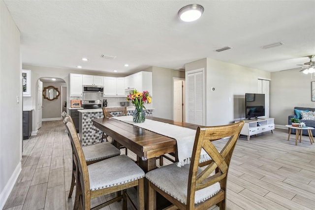 dining space featuring wood finish floors, visible vents, arched walkways, and ceiling fan