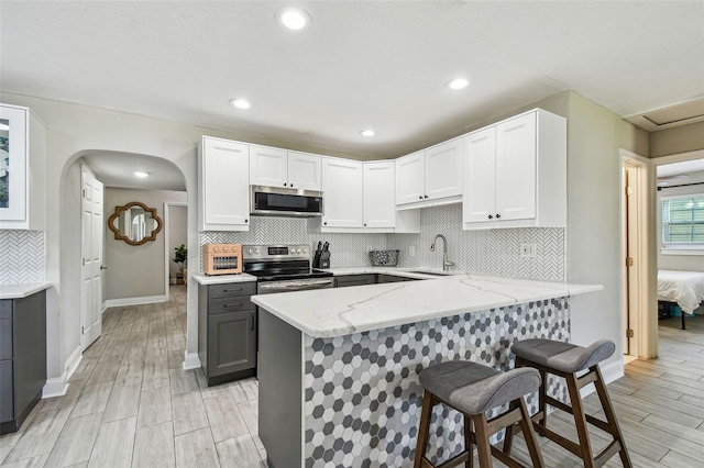 kitchen featuring light stone counters, gray cabinets, a sink, appliances with stainless steel finishes, and a kitchen bar