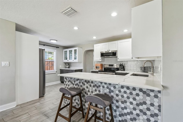 kitchen with visible vents, a peninsula, arched walkways, a sink, and stainless steel appliances