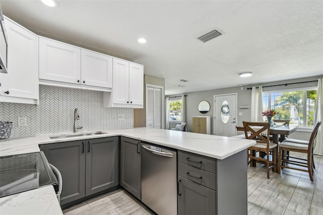 kitchen featuring visible vents, gray cabinetry, a sink, stainless steel dishwasher, and a peninsula