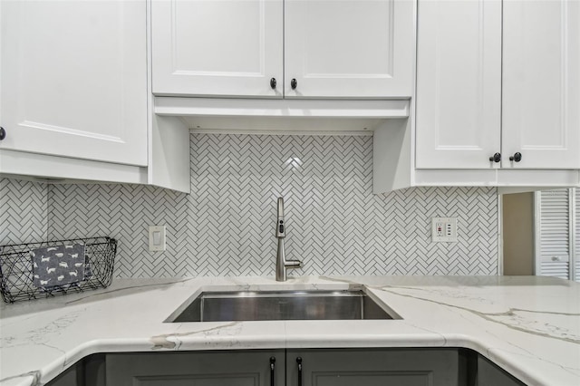 kitchen with tasteful backsplash, white cabinets, light stone countertops, and a sink