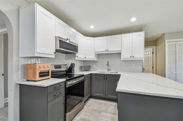 kitchen featuring light stone countertops, a peninsula, gray cabinets, a sink, and appliances with stainless steel finishes