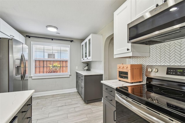 kitchen featuring light stone counters, stainless steel appliances, white cabinets, and decorative backsplash