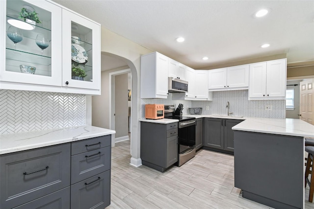 kitchen with gray cabinetry, a sink, light stone counters, stainless steel appliances, and arched walkways