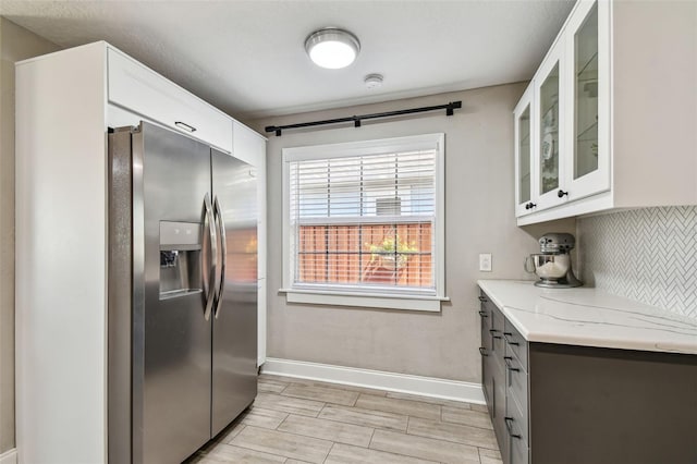 kitchen featuring glass insert cabinets, stainless steel fridge, white cabinets, decorative backsplash, and baseboards