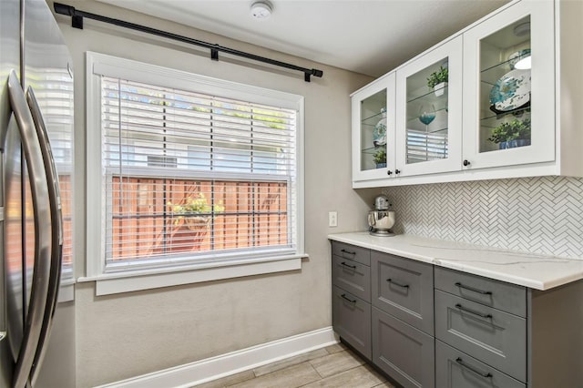 kitchen with backsplash, glass insert cabinets, baseboards, gray cabinets, and freestanding refrigerator