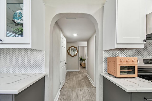 hallway with light wood-style flooring, a toaster, baseboards, and arched walkways