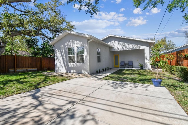 rear view of property featuring a patio area, a yard, fence, and stucco siding