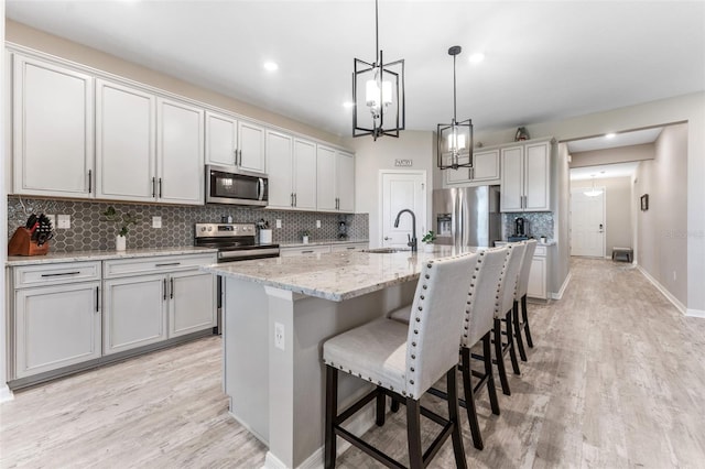 kitchen with a kitchen bar, decorative backsplash, light wood-style floors, stainless steel appliances, and a sink