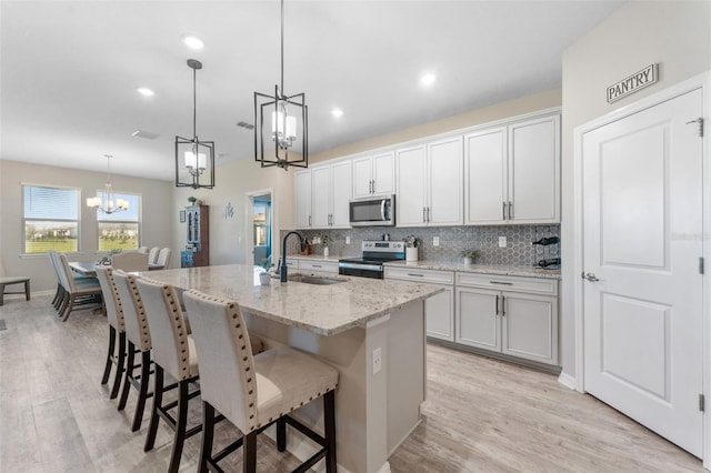 kitchen featuring a center island with sink, a sink, stainless steel appliances, a notable chandelier, and tasteful backsplash