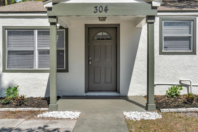 view of exterior entry featuring a shingled roof and stucco siding