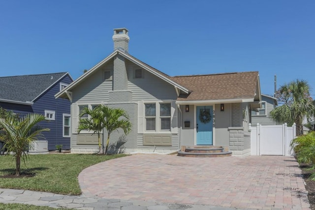 view of front of house featuring a gate, fence, roof with shingles, a front yard, and a chimney