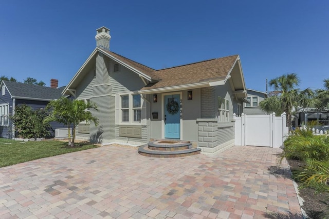 view of front of home featuring a shingled roof, a gate, fence, and a chimney