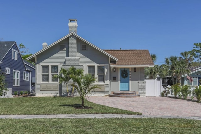 bungalow-style home with a chimney, fence, a front yard, and roof with shingles