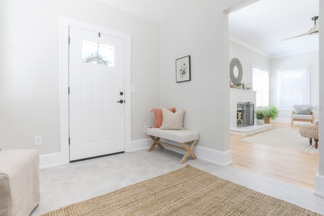 entryway with a fireplace with raised hearth, crown molding, and baseboards