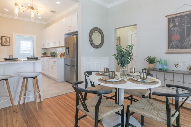 dining room with light wood-type flooring, visible vents, ornamental molding, and a chandelier