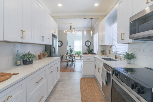 kitchen featuring a sink, stainless steel appliances, an inviting chandelier, white cabinets, and crown molding