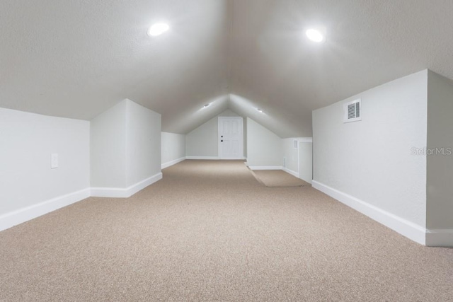 bonus room featuring visible vents, light carpet, lofted ceiling, a textured ceiling, and baseboards