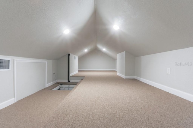 additional living space featuring visible vents, lofted ceiling, a textured ceiling, and carpet flooring