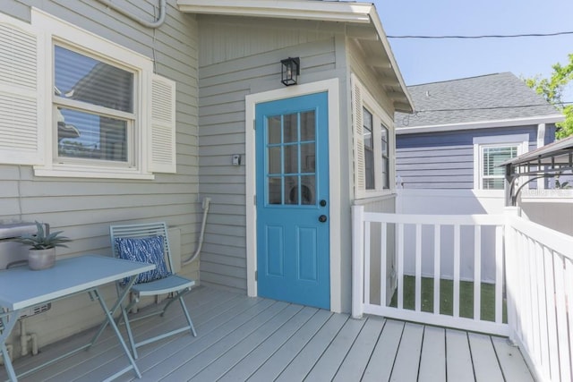 property entrance featuring roof with shingles and a wooden deck