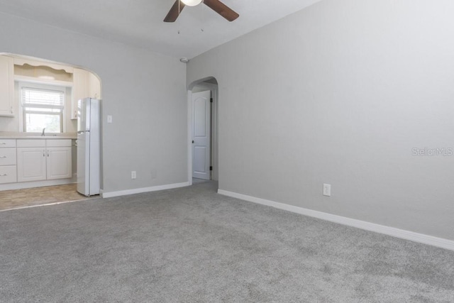 unfurnished bedroom featuring baseboards, light colored carpet, freestanding refrigerator, arched walkways, and a sink