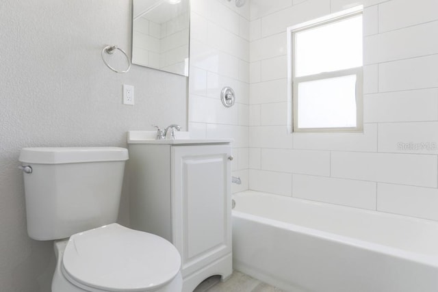 bathroom with washtub / shower combination, toilet, vanity, and a textured wall