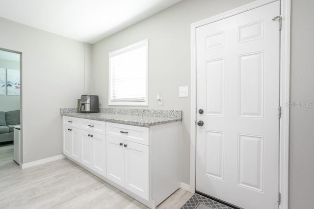 kitchen featuring light stone counters, baseboards, light wood finished floors, and white cabinetry