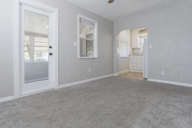 interior space with baseboards, arched walkways, light colored carpet, and ceiling fan