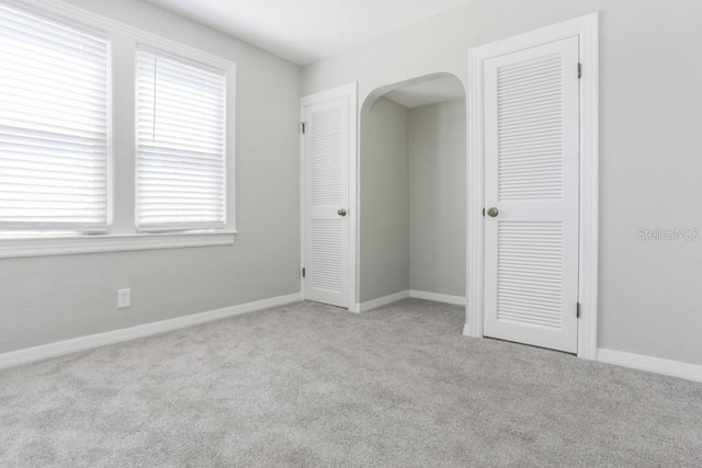 empty room featuring carpet flooring, arched walkways, and baseboards