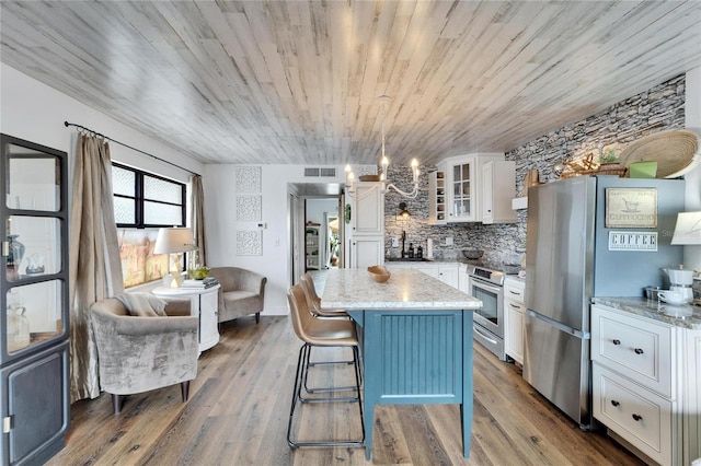 kitchen with a kitchen island, wood finished floors, white cabinetry, appliances with stainless steel finishes, and glass insert cabinets