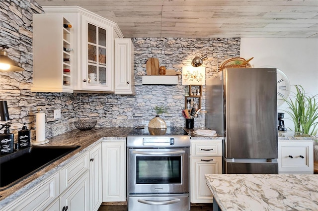 kitchen with light stone counters, glass insert cabinets, appliances with stainless steel finishes, and white cabinetry