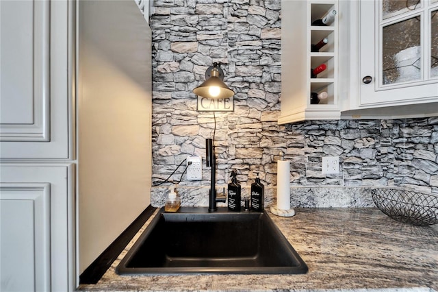 kitchen featuring white cabinetry, decorative backsplash, glass insert cabinets, and a sink