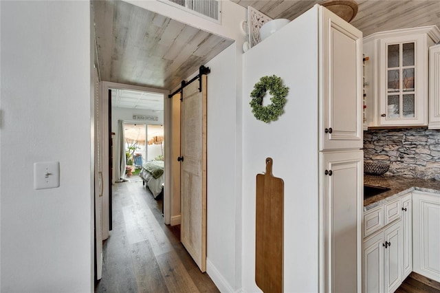 hallway with a barn door, dark wood-type flooring, and visible vents