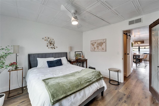 bedroom with a barn door, baseboards, visible vents, and wood finished floors