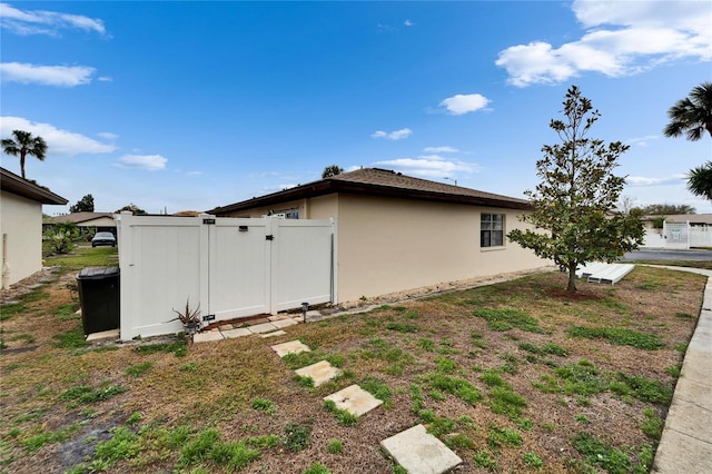 view of side of property featuring stucco siding, fence, and a gate